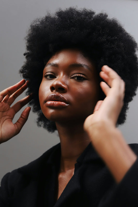 Black woman with an afro and glossy lips posing with her hands raised