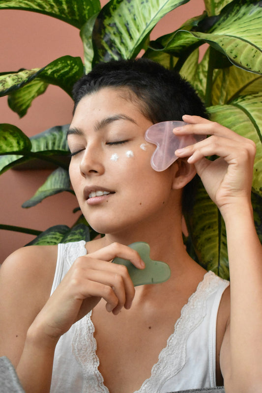 Woman holding a green stone gua sha tool as part of her skincare routine