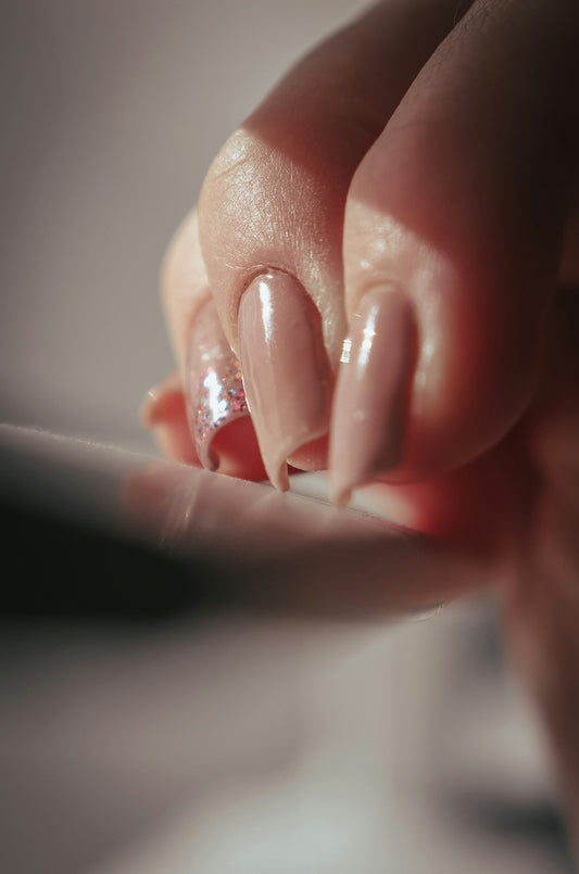 Brown-skinned woman's hand with a glitter manicure in sunlight