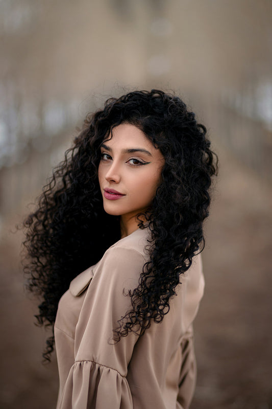 Woman with long black curly hair posing against a gray background